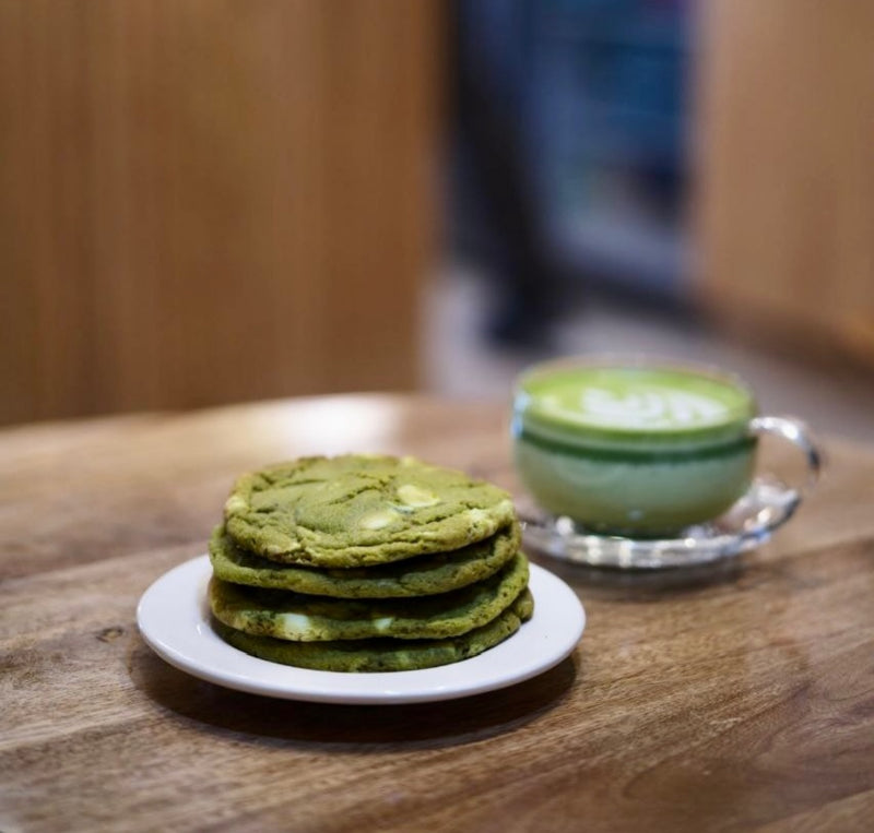 Stack of green cookies on a plate with a cup of matcha latte in the background.